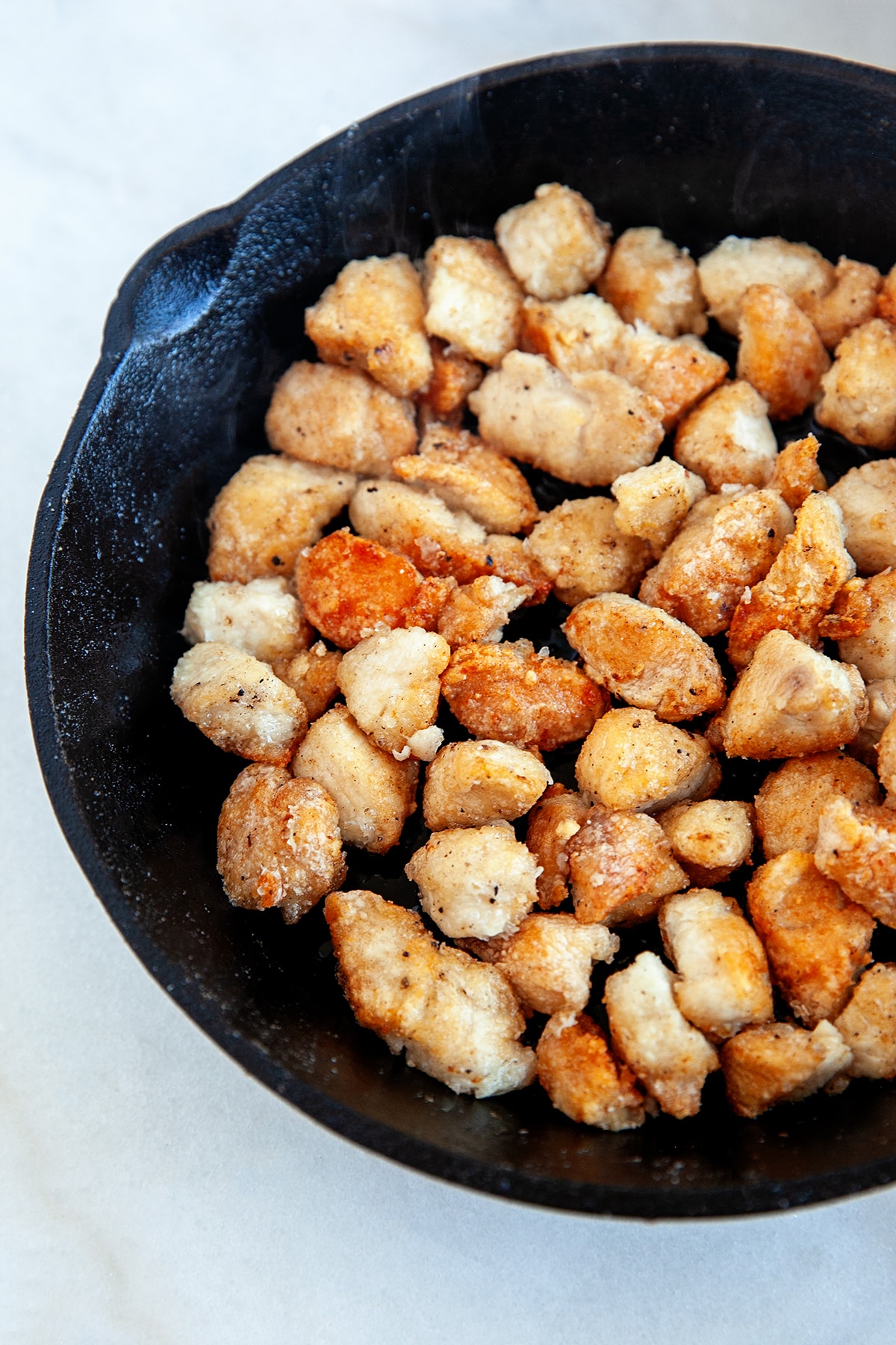 Frying up small cubes of chicken in cornstarch in a cast iron pan. 