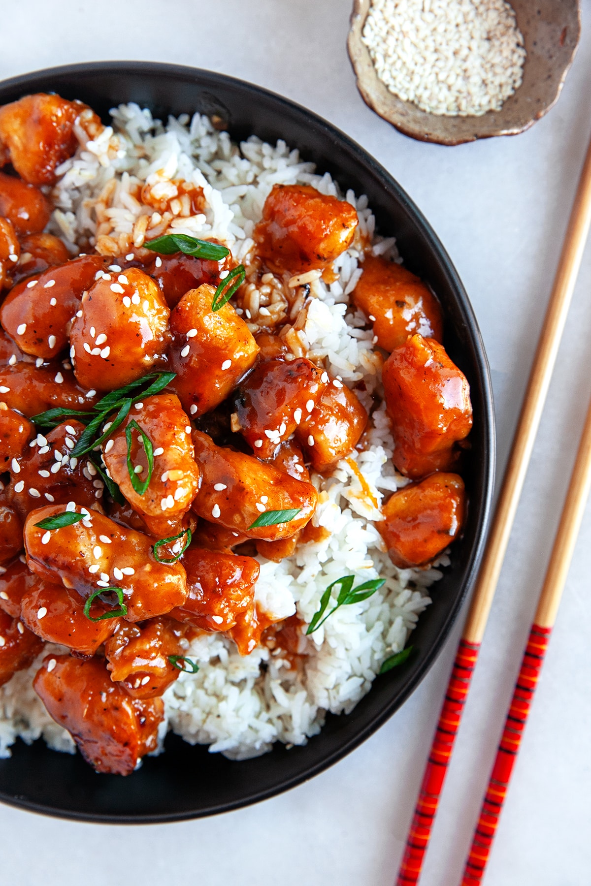 Overhead shot of Orange Chicken over rice on a black plate. 