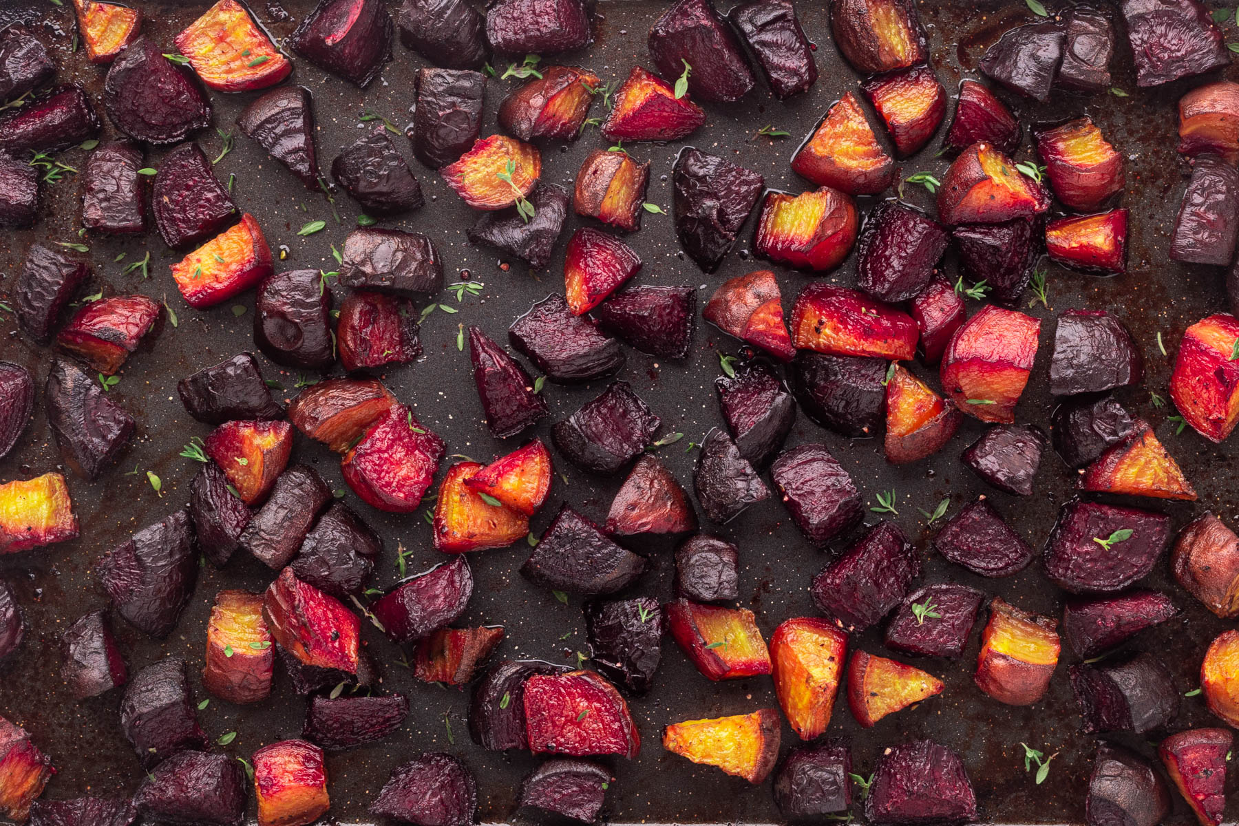 Overhead of a panful of roasted beets with a sprinkle of thyme leaves. 