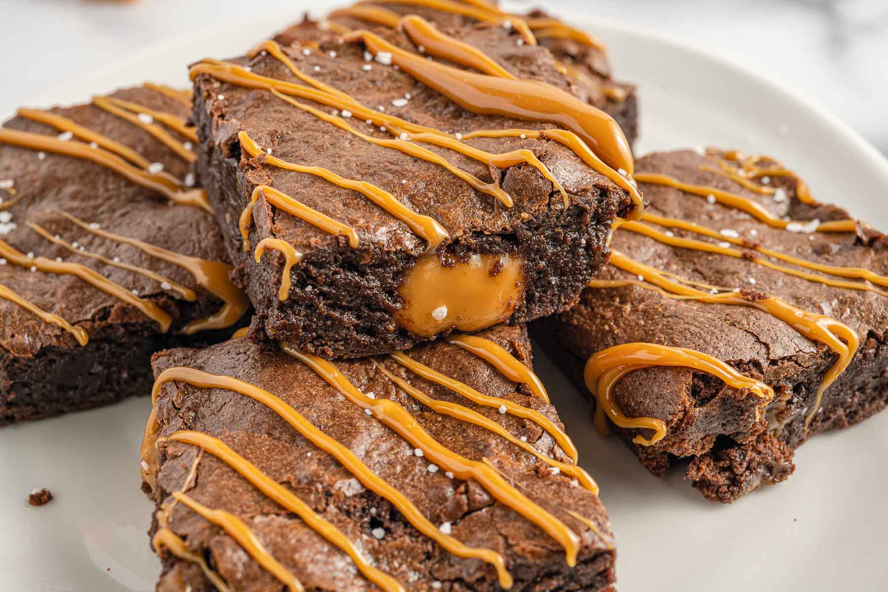 Horizontal photo of brownies drizzled with caramel and one oozing with caramel. 