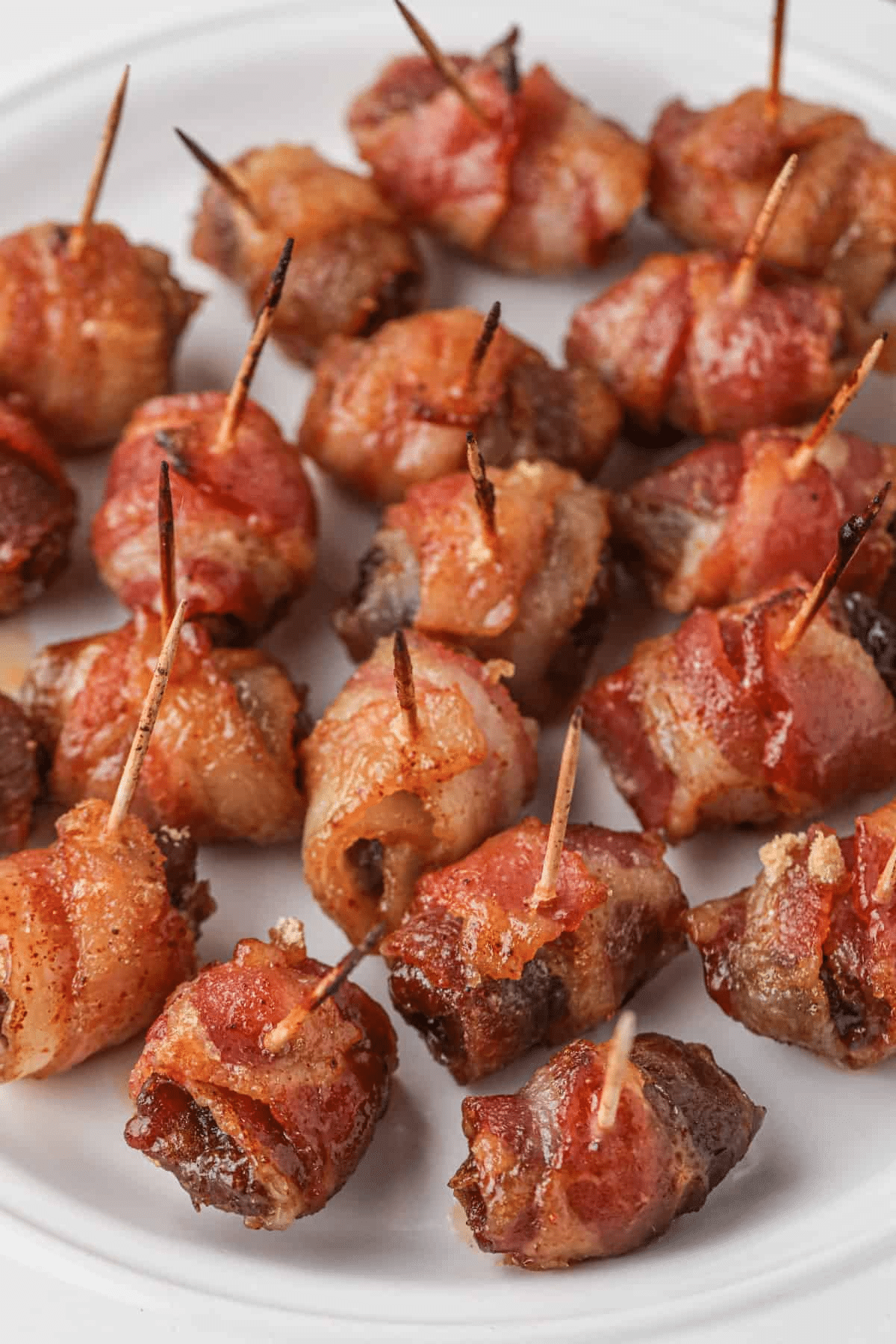 Bacon-Wrapped Dates with toothpicks on a white plate. 