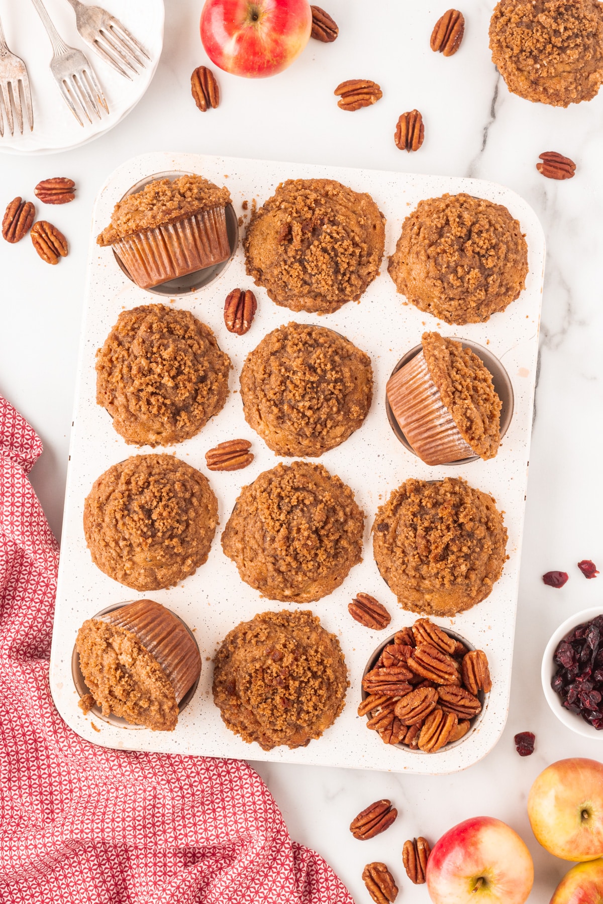 Overhead of muffins in a tin with pecans in one of the holes and scattered about. 