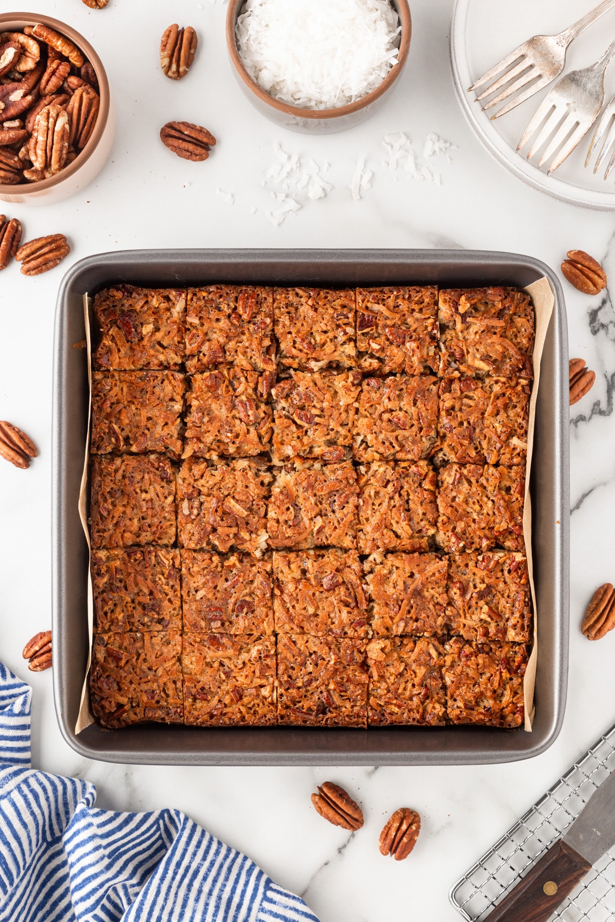 Pecan bars cut into small squares in a baking pan with parchment. 