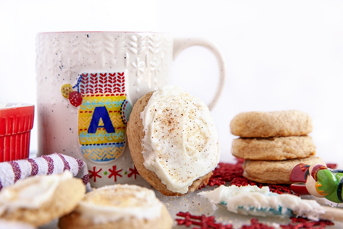 Horizontal photo with a cookie leaning against a mug and others stacked around it. 
