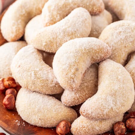 Stacked crescent cookies on a board with hazelnuts.