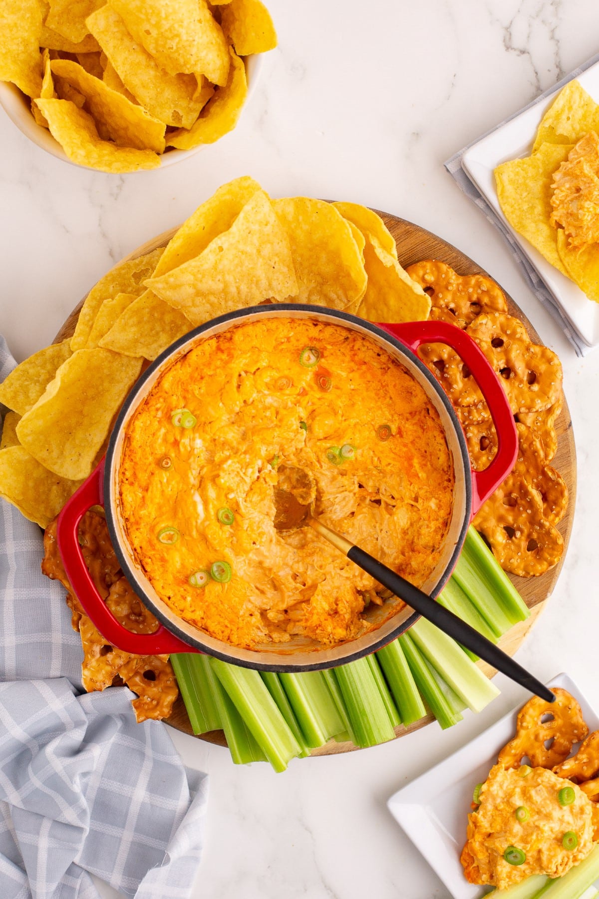 A spoon in the Buffalo Chicken Dip Recipe surrounded by chips and celery. 