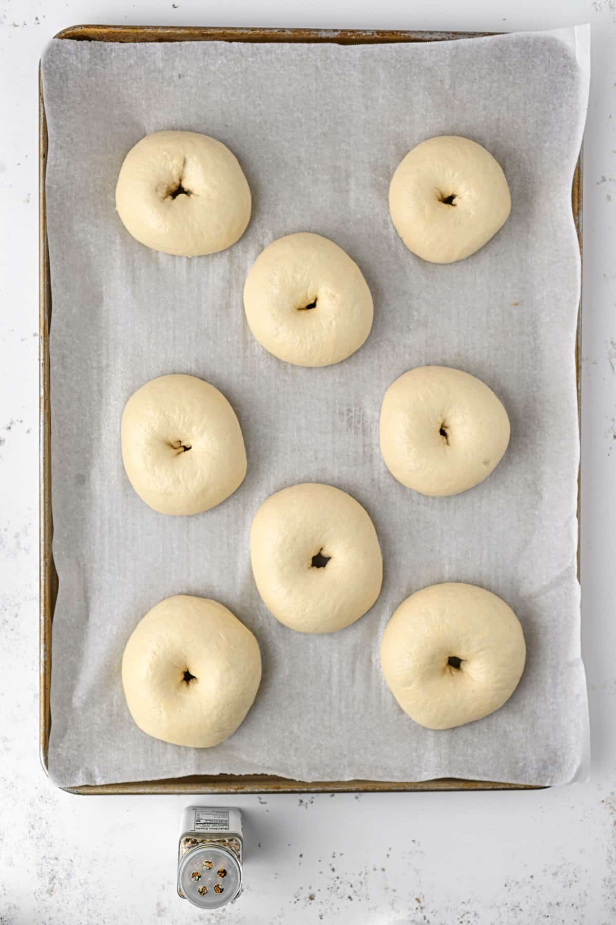 Bagels have risen on a baking sheet with parchment. 