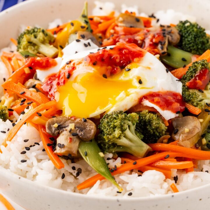 Close-up plate of stir-fry over rice with a poached egg.