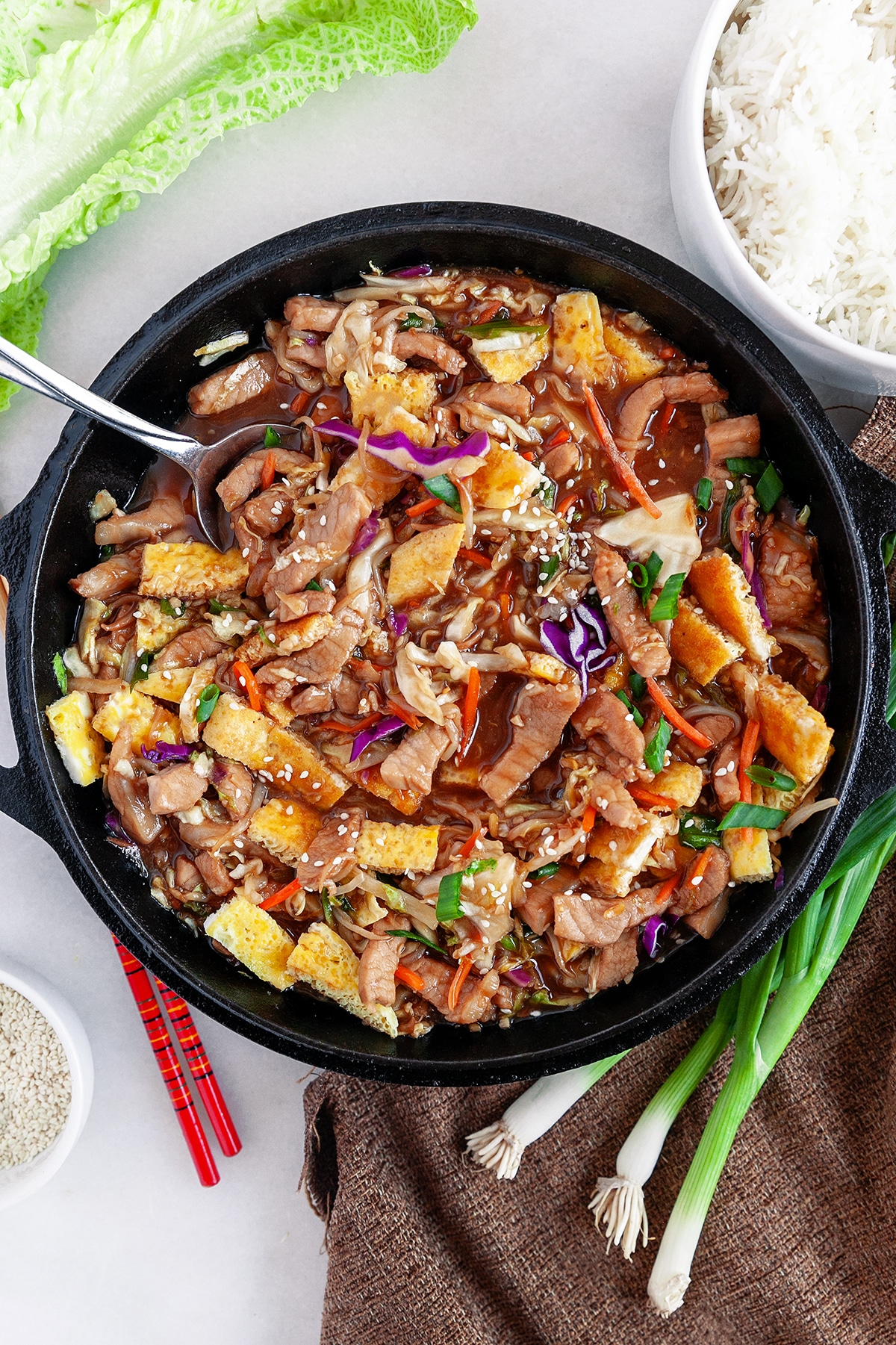 Overhead of Moo Shu Pork in a cast iron pan with a spoon. 