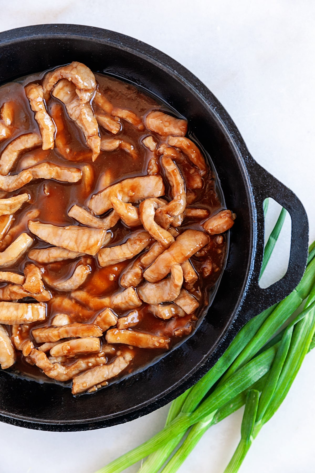 Pork strips in sauce in a cast iron pan. 