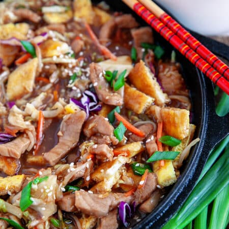 Overhead close-up of moo shu pork in a cast iron pan with chopsticks on the side.