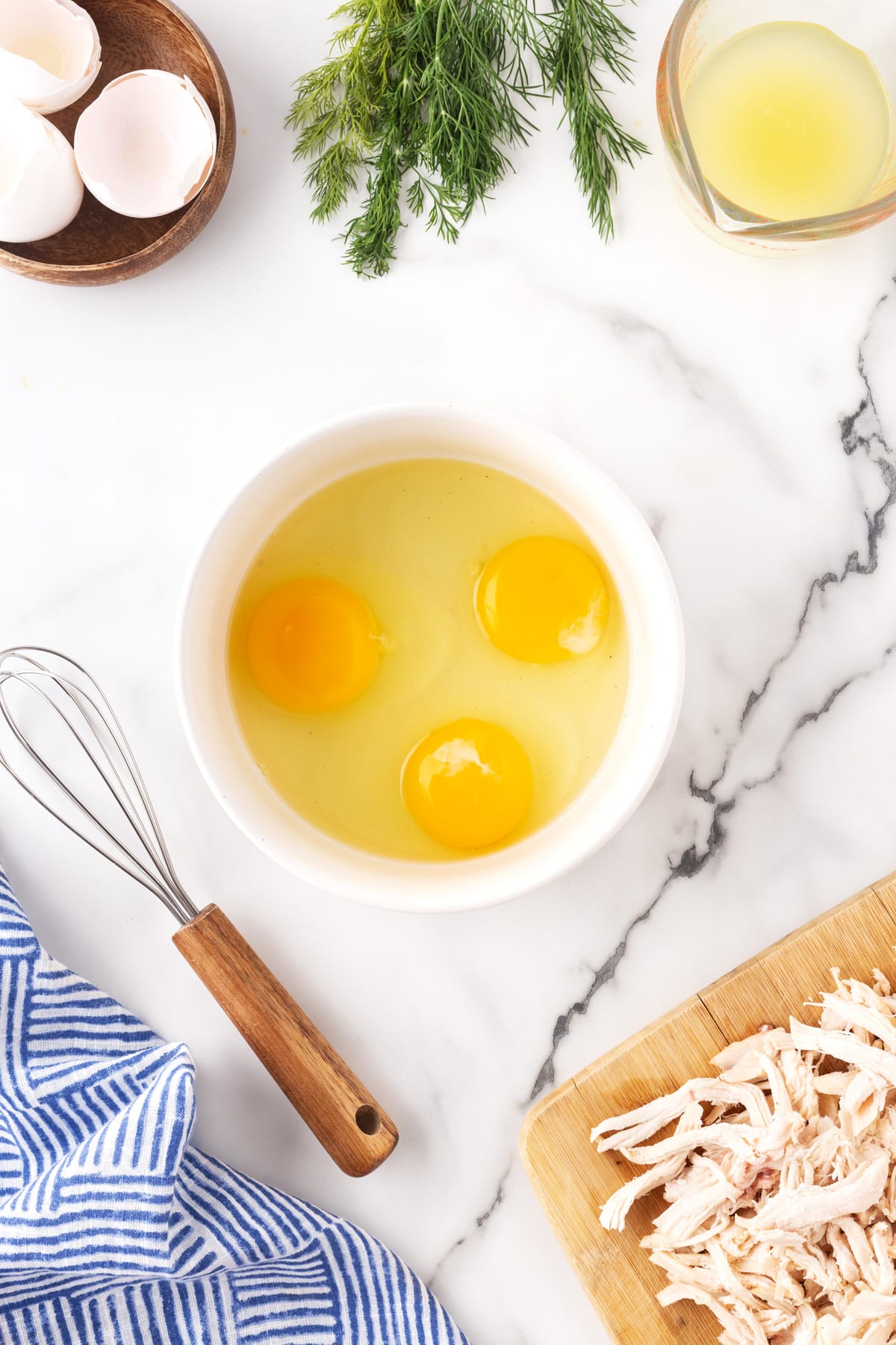 Eggs in a bowl with a whisk beside them. 