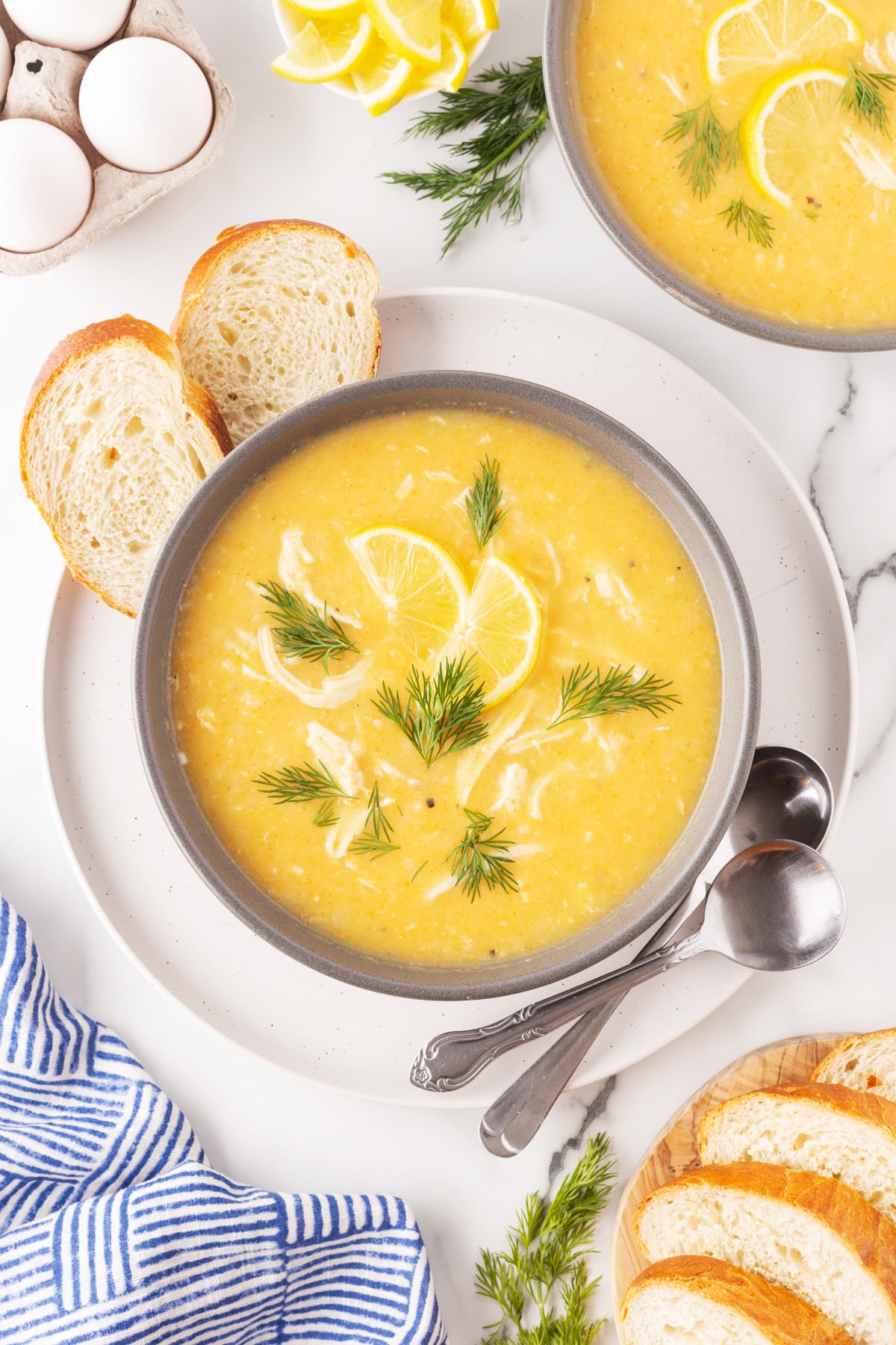 Bowls of Avgolemono Soup with eggs, lemon slices and bread. 