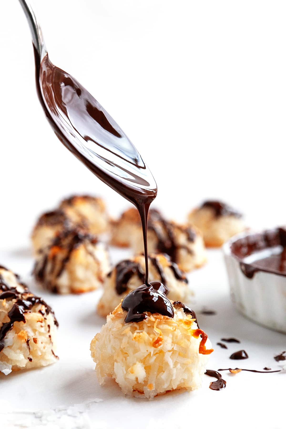 Showing a spoon drizzling on chocolate to a macaroon. 