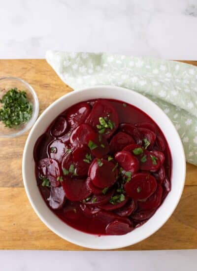 Harvard beets in a bowl on a board topped with parsley.