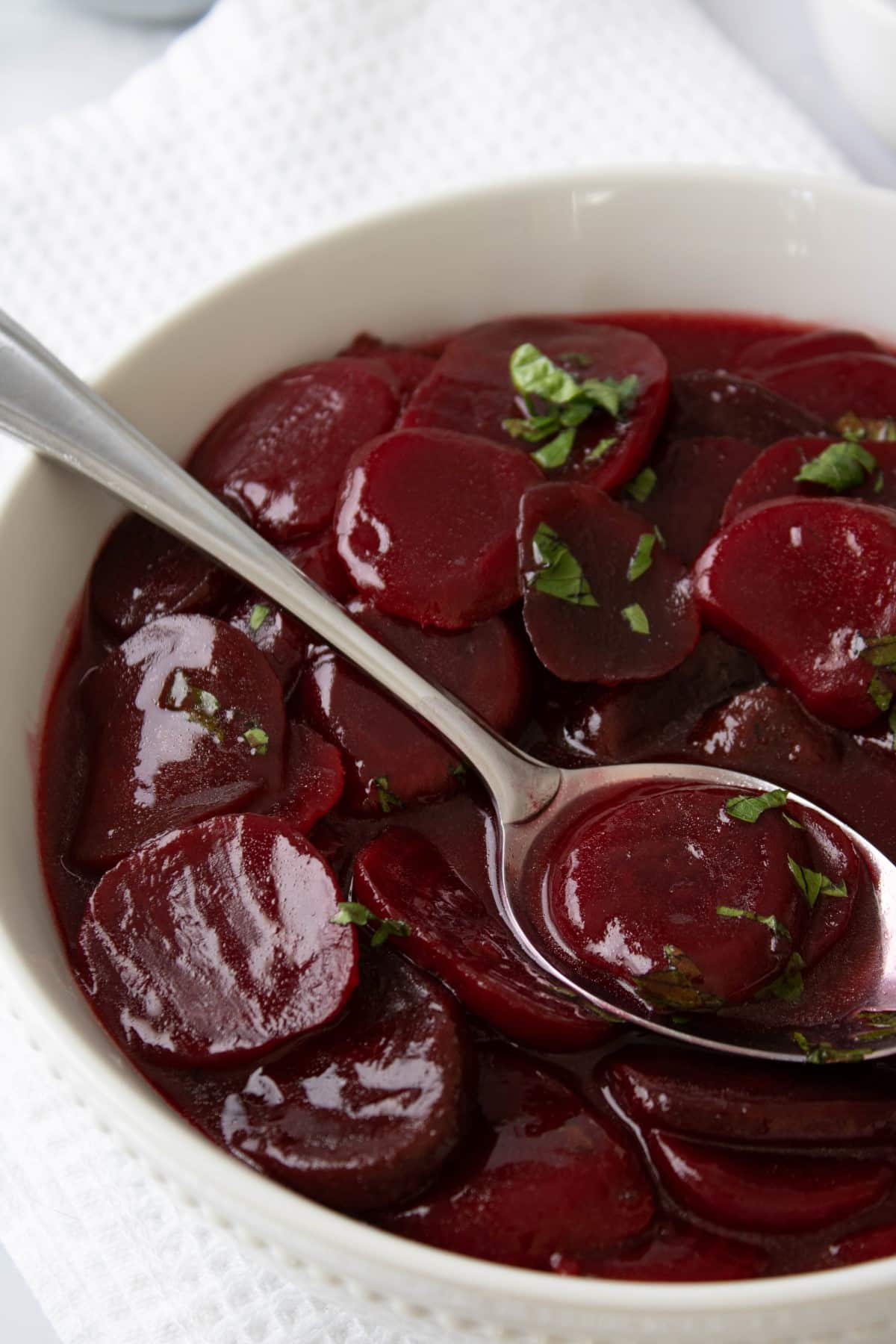 A bowl full of sliced beets in a sauce with a spoon. 