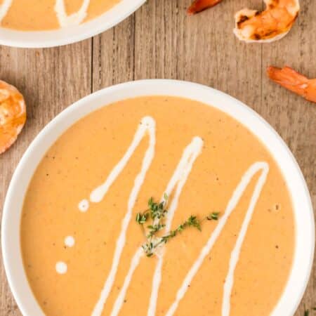 Overhead showing bowls of shrimp bisque with cream drizzled on top.