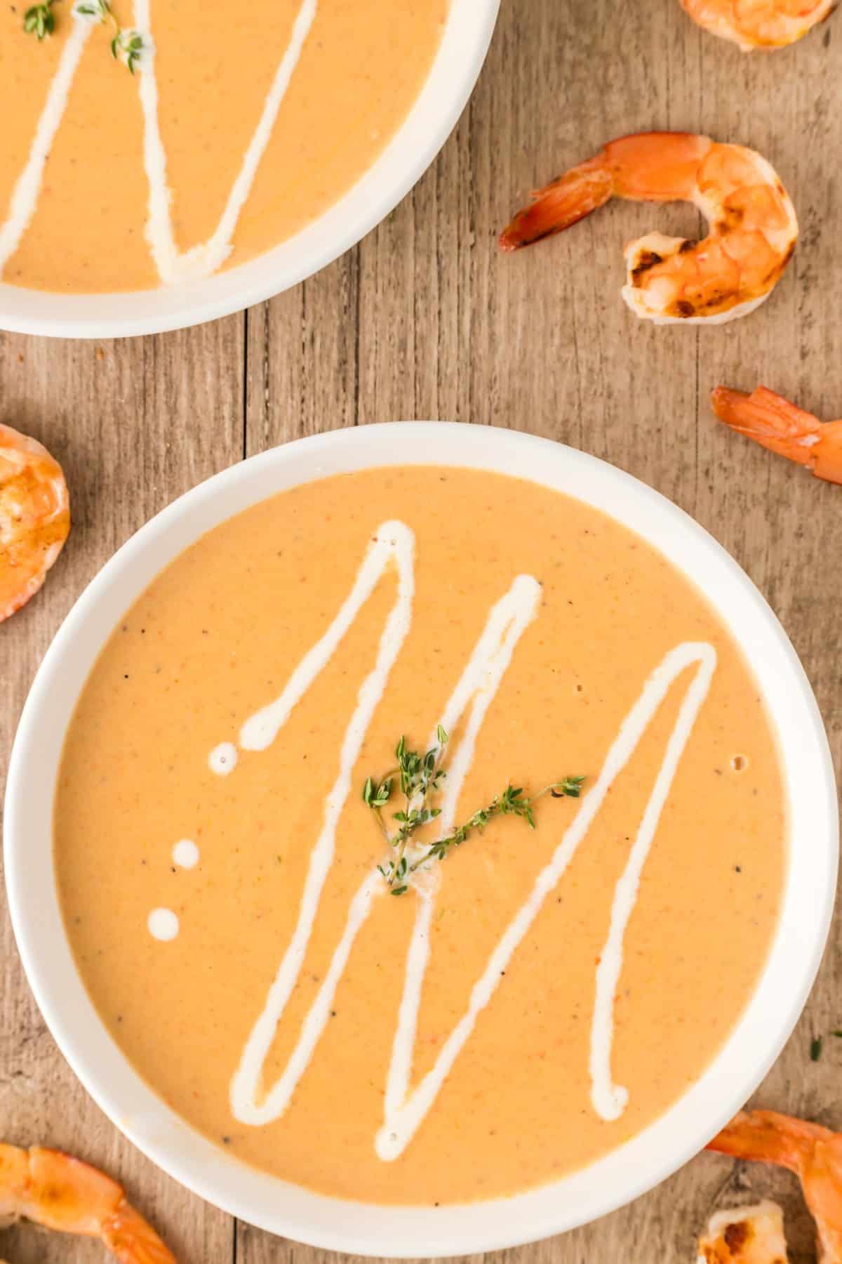 Overhead shot of shrimp bisque in bowls drizzled with cream and a fresh thyme sprig. 