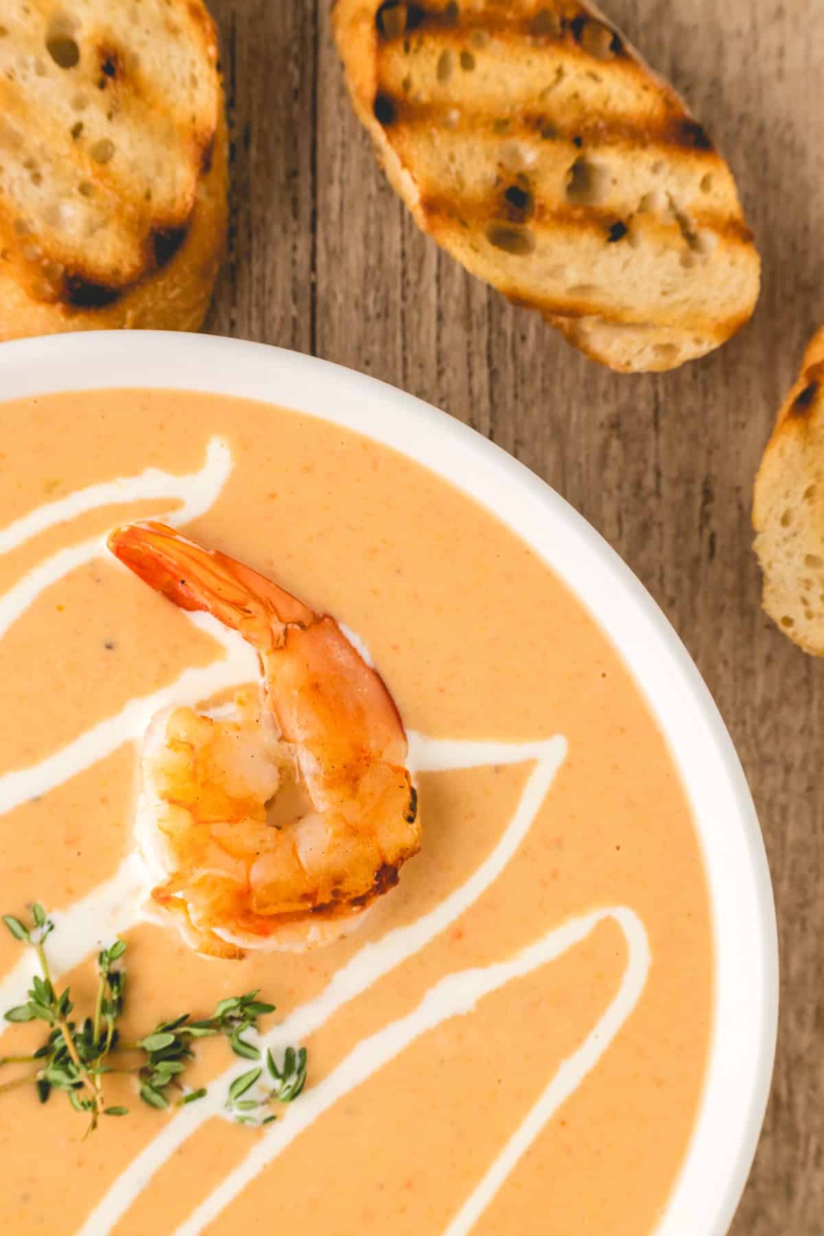 Showing a shrimp to the side of a bowl of soup with fresh thyme also. 
