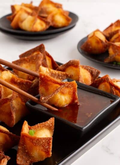 Crab Rangoon in chopsticks being dipped in sauce.