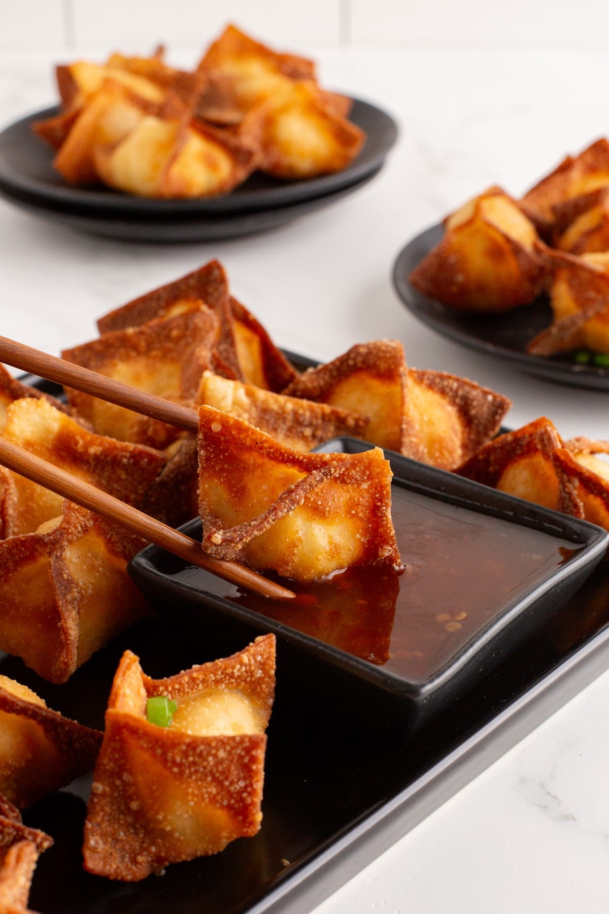 Crab Rangoon on chop sticks being dipped into a dipping sauce.