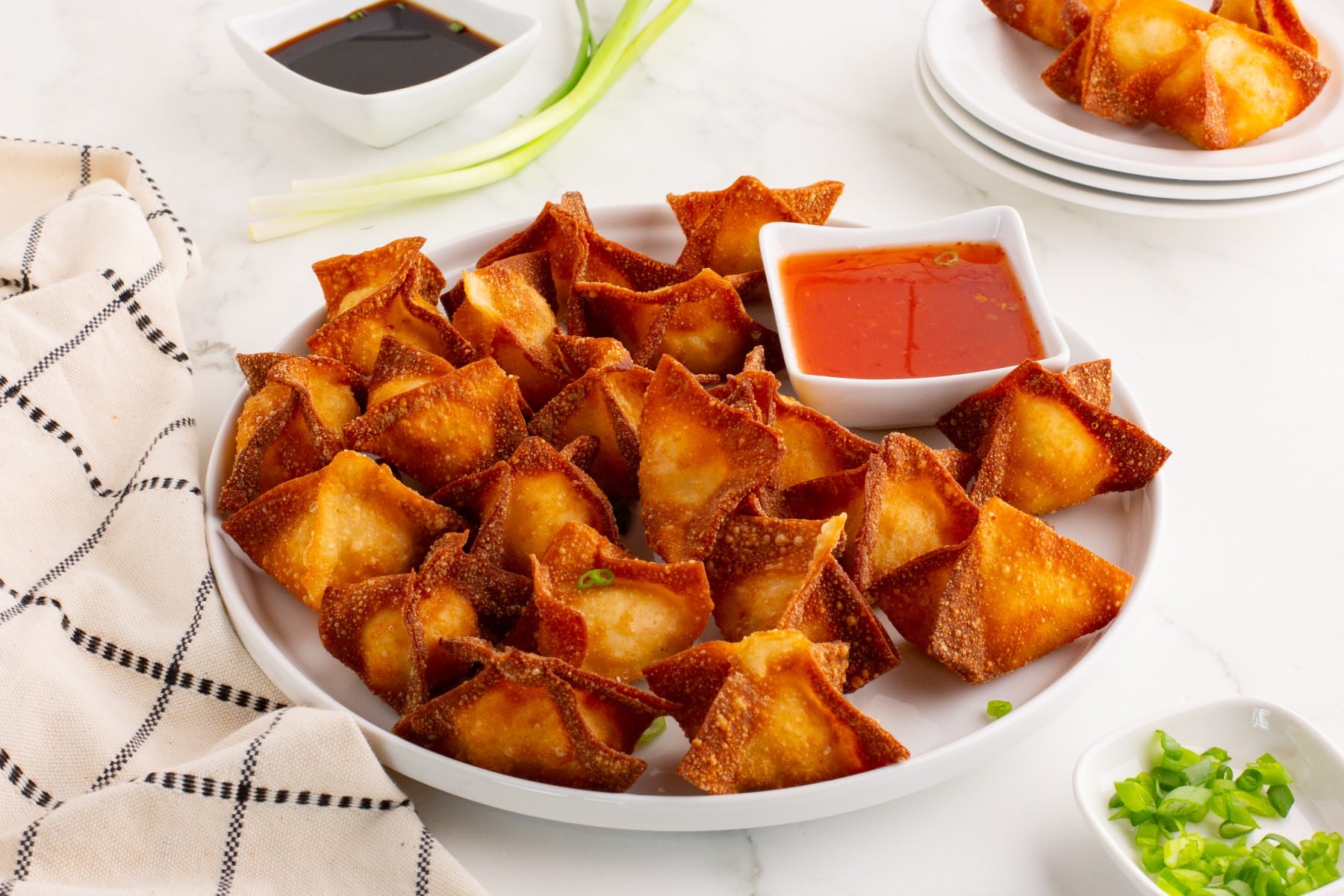 Crab rangoon served on a white platter with a bowl of dipping sauce.