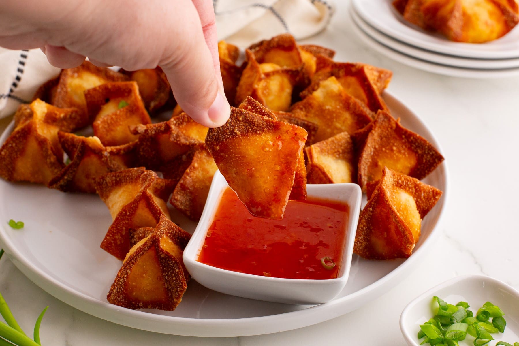 Crab Rangoon wonton held in 2 fingers being dipped into a dipping sauce.