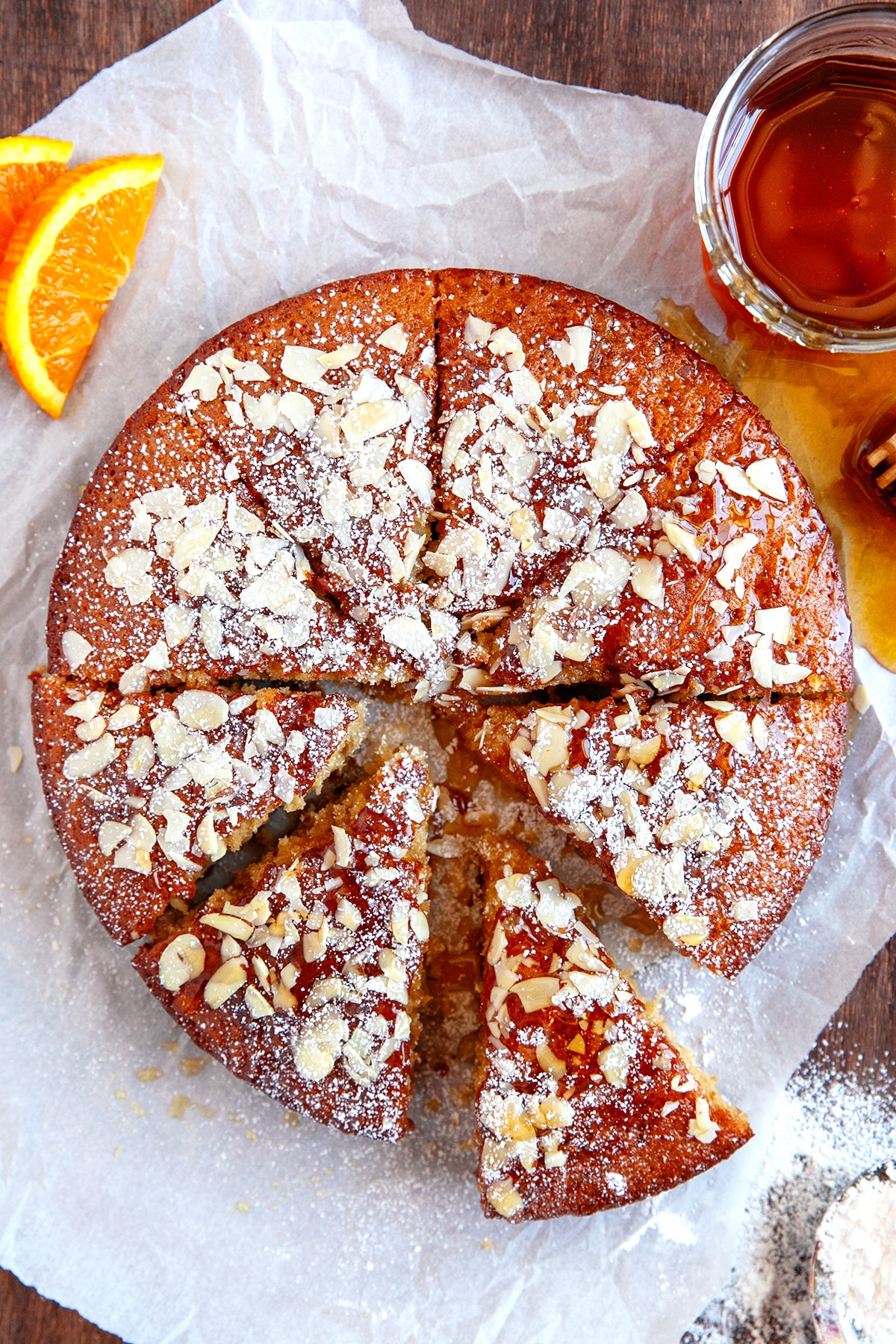 Overhead shot of honey cake that has been dusted with powdered sugar, sliced almonds and drizzled with honey. 