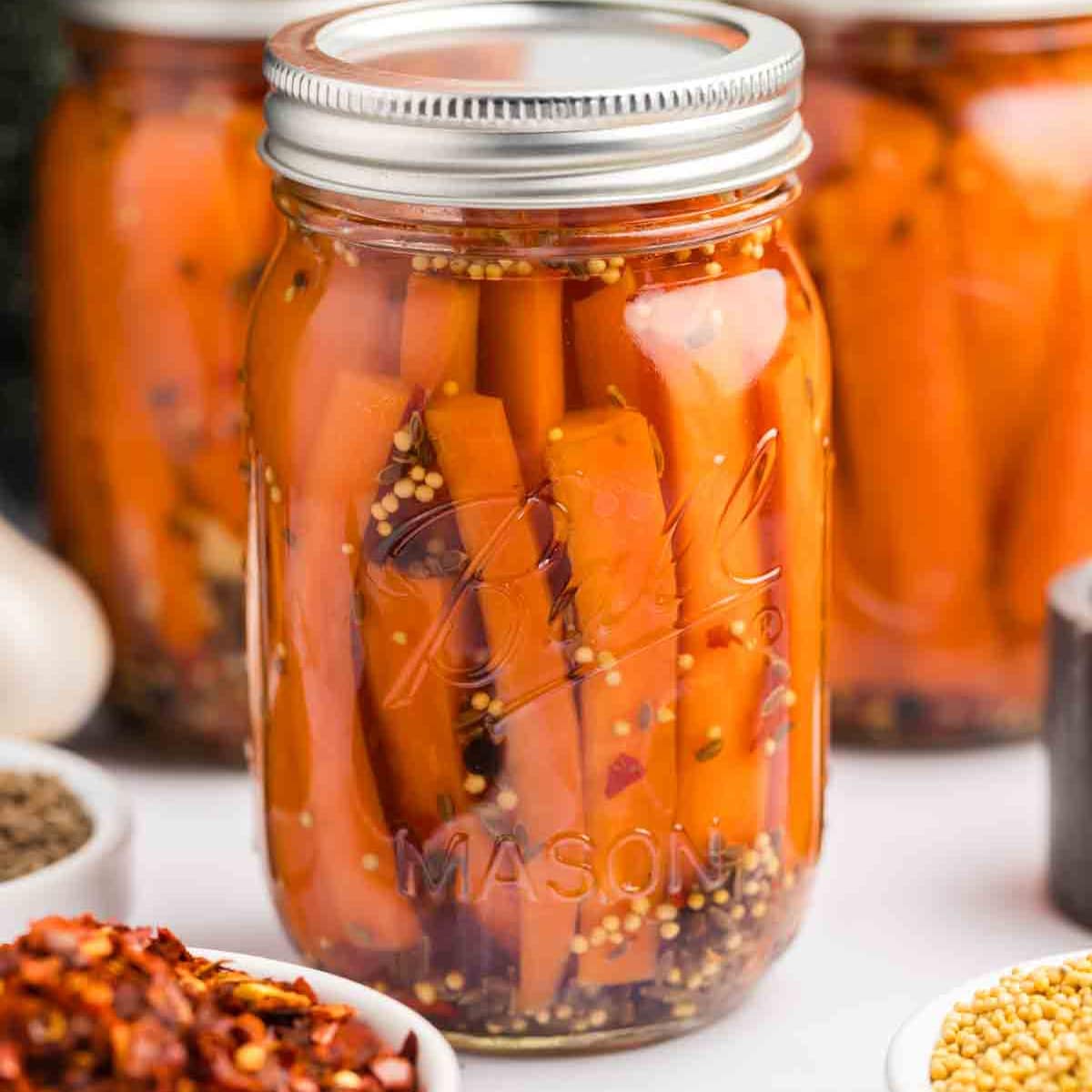 Square photo of a close-up of pickled carrots in a jar. 