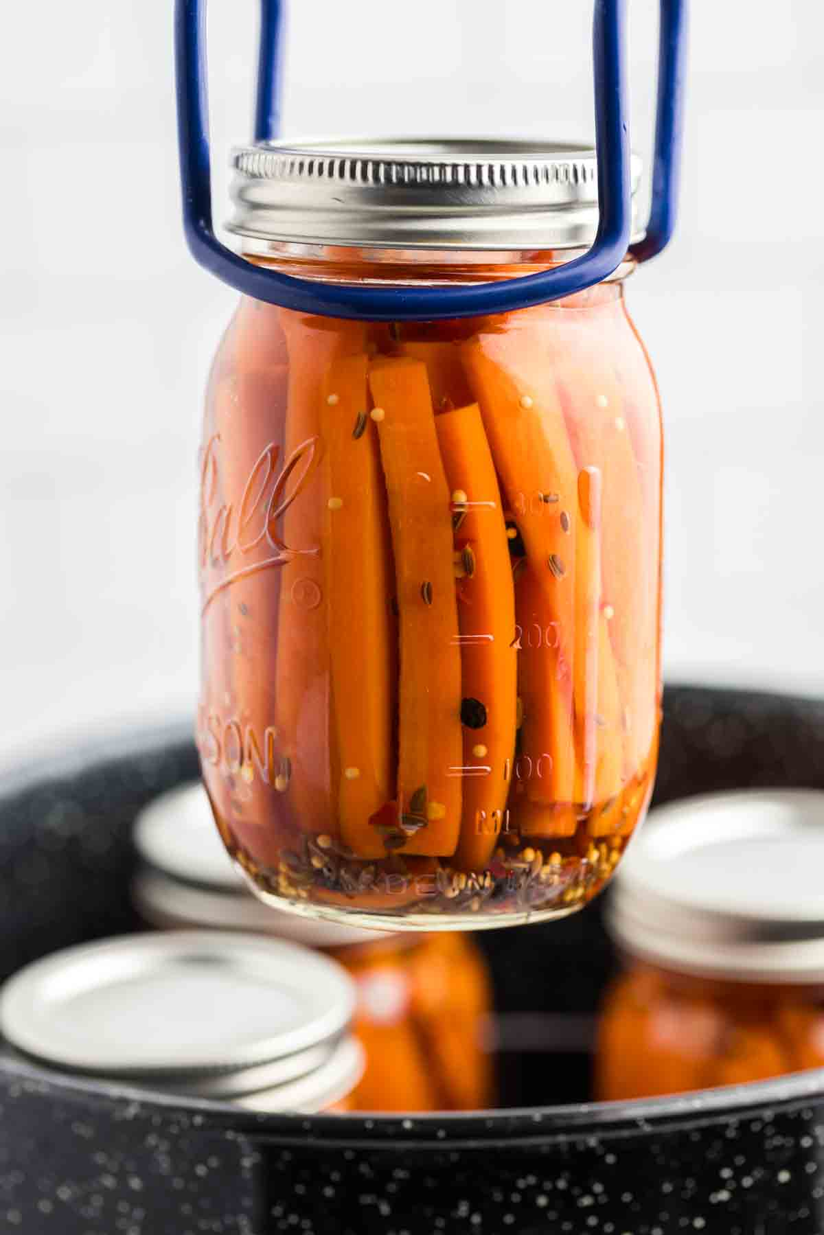 Pulling a jar of carrots out of the water bath with a jar lifter. 