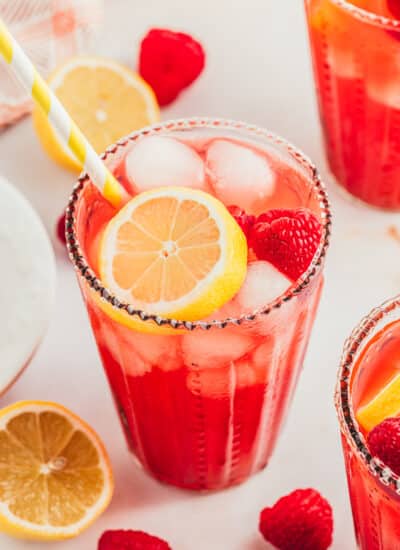 Raspberry Lemonade in a tall glass garnished with fresh raspberries and lemon slice.