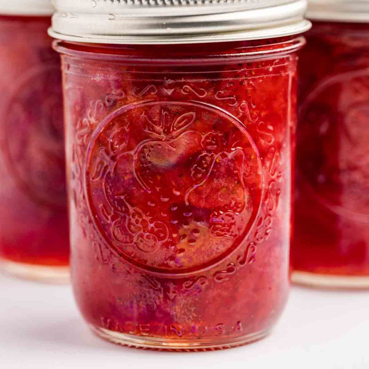 Square photo of jars of strawberry jam. 