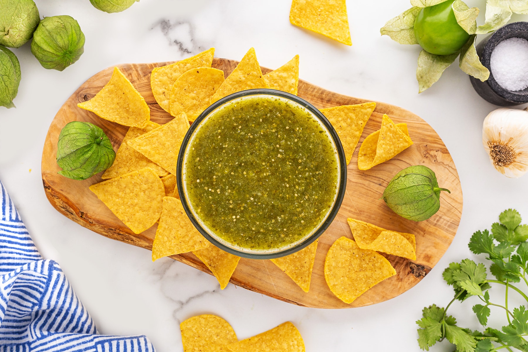 Horizontal shot of salsa verde on a board with tortillas chips and surrounded by the other ingredients.. 