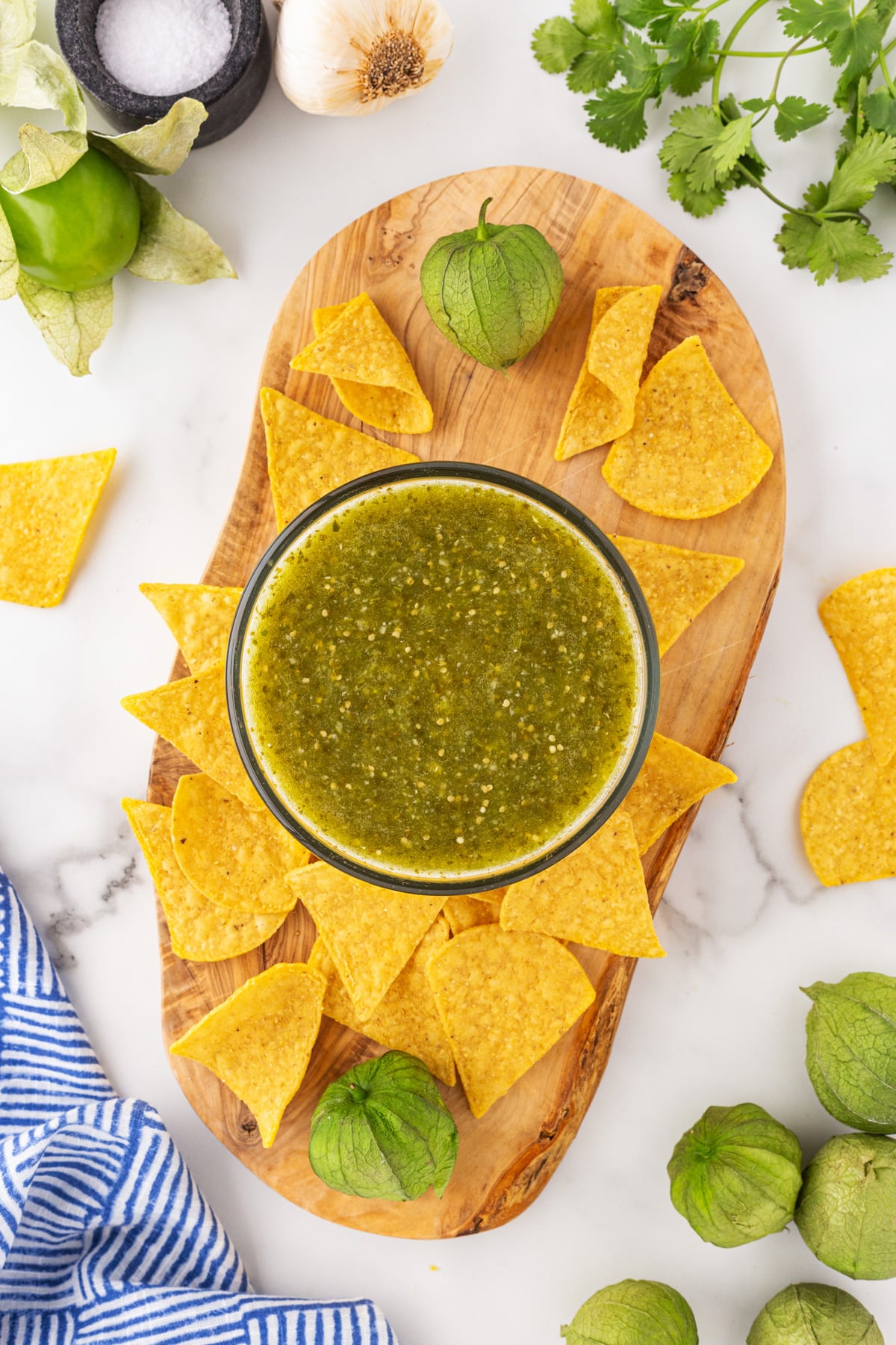 Tomatillo Green Chili Salsa on a board with tortilla chips and other ingredients surrounding it. 
