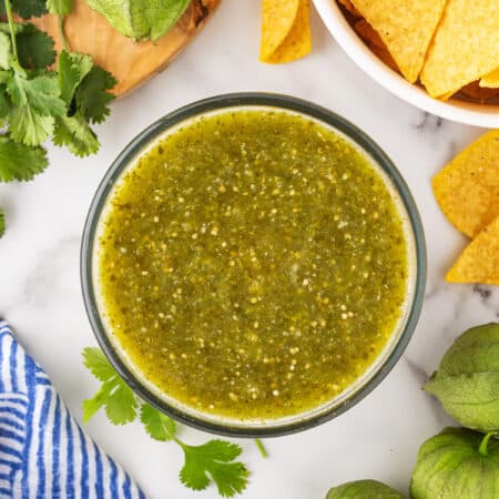 Overhead shot of Tomatillo Green Chili Salsa in a bowl with tortilla chips and tomatillos on the side.