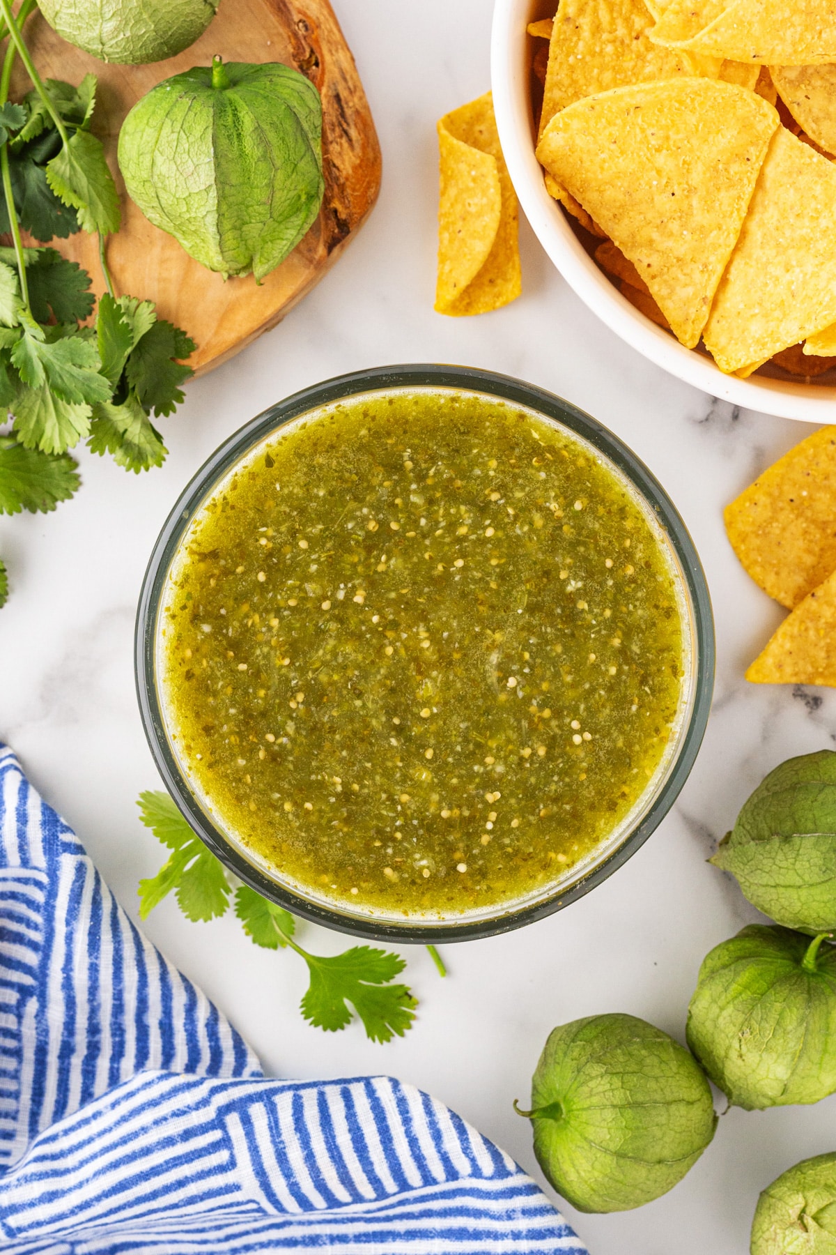 Overhead shot of Tomatillo Green Chili Salsa in a bowl with tortilla chips and tomatillos on the side.