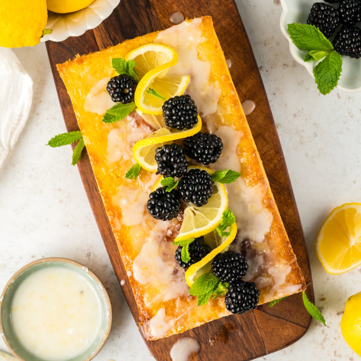 Square photo of a lemon blackberry cake taken from overhead decorated with blackberries, lemon and mint. 