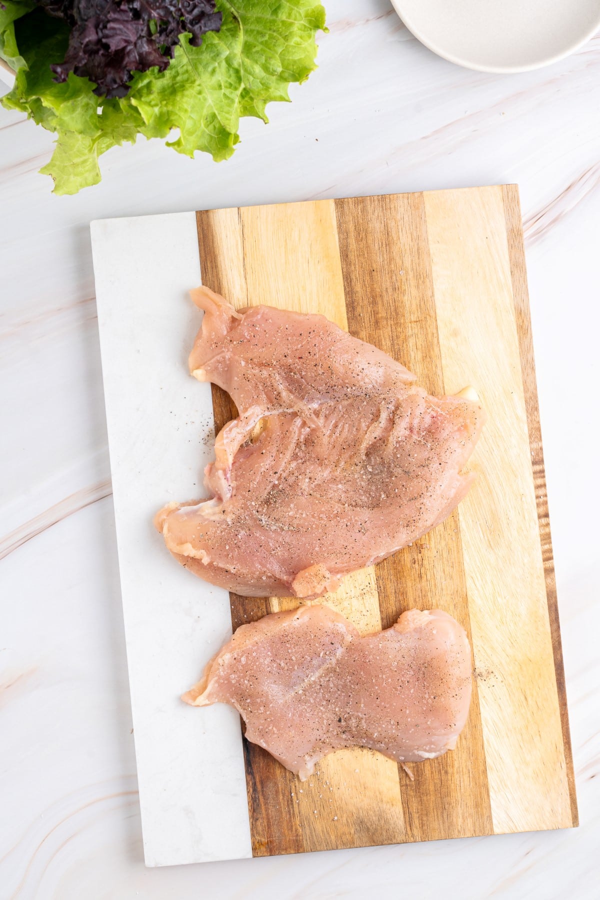 Thin chicken filets, seasoned on a cutting board. 