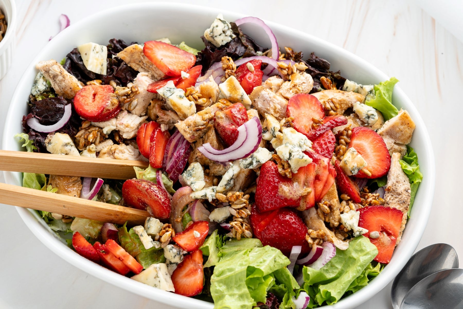 Horizontal bowl of salad with wood tongs. 