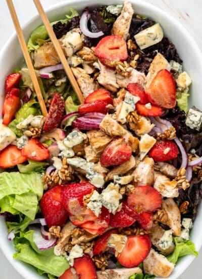 Oval bowl of strawberry chicken salad with tongs.