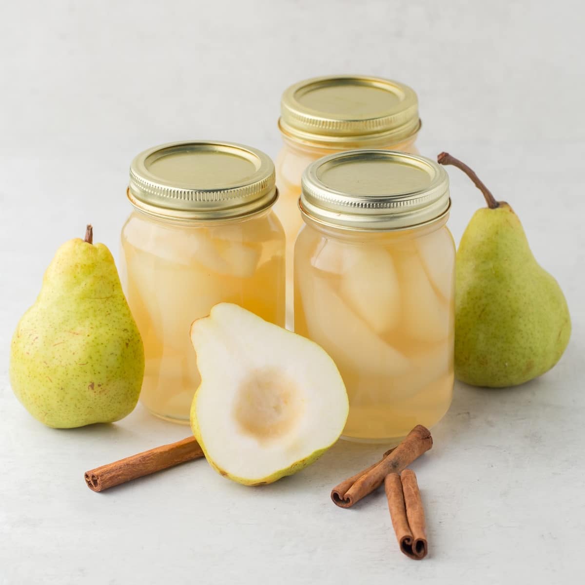 Three jars of pears plus whole pears, half a pear and cinnamon sticks. 