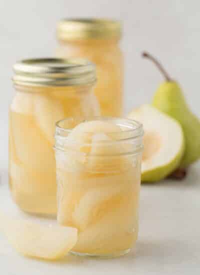 Jars of pears with one open and fresh pears in the background.