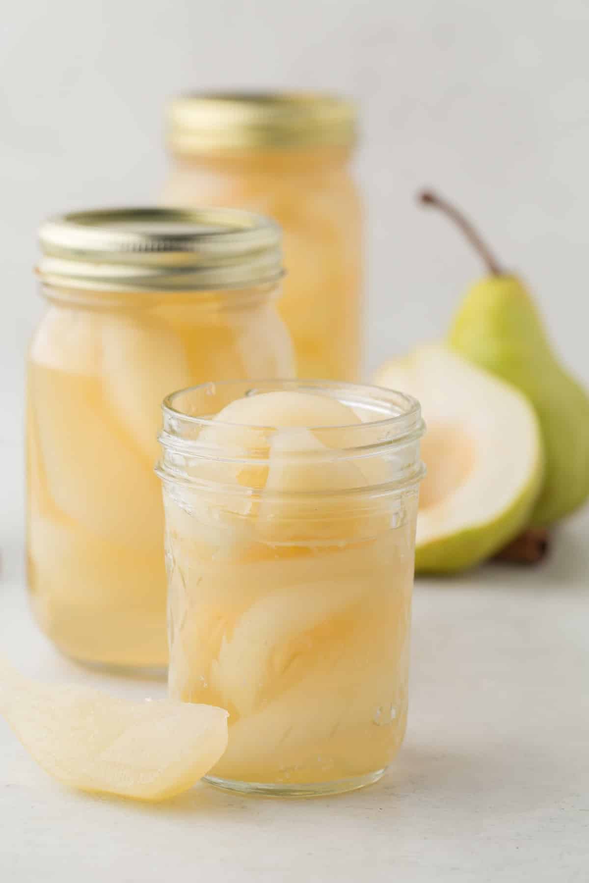 Canned pear jars of various sizes and a whole and sliced pear in the background. 