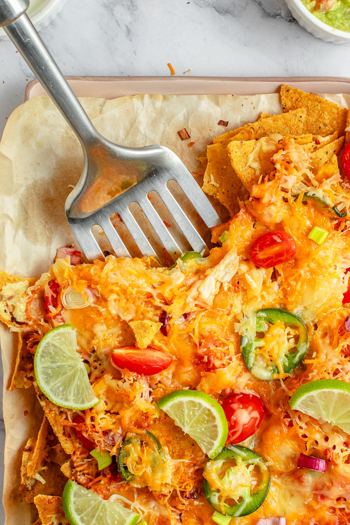 Chicken Nachos being served with a metal spatula from the baking sheet. 