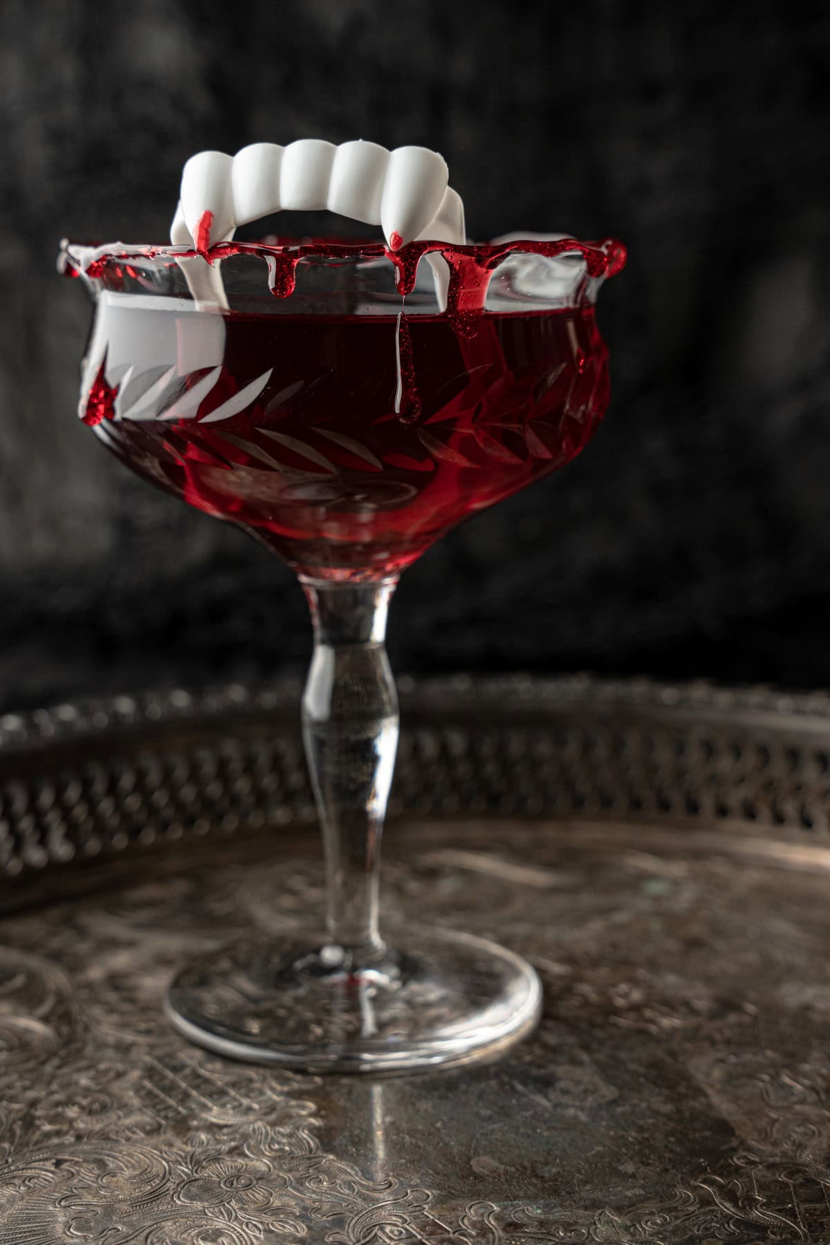 Cocktail glass filled with Dracula's Kiss Cocktail and topped with fake vampire teeth. 