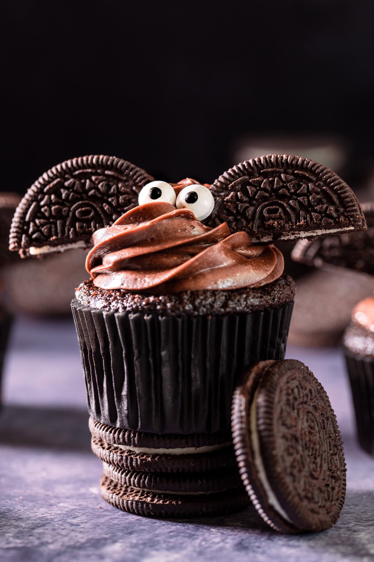 A chocolate bat cupcake on a counter sitting on top of two Oreo cookies. 