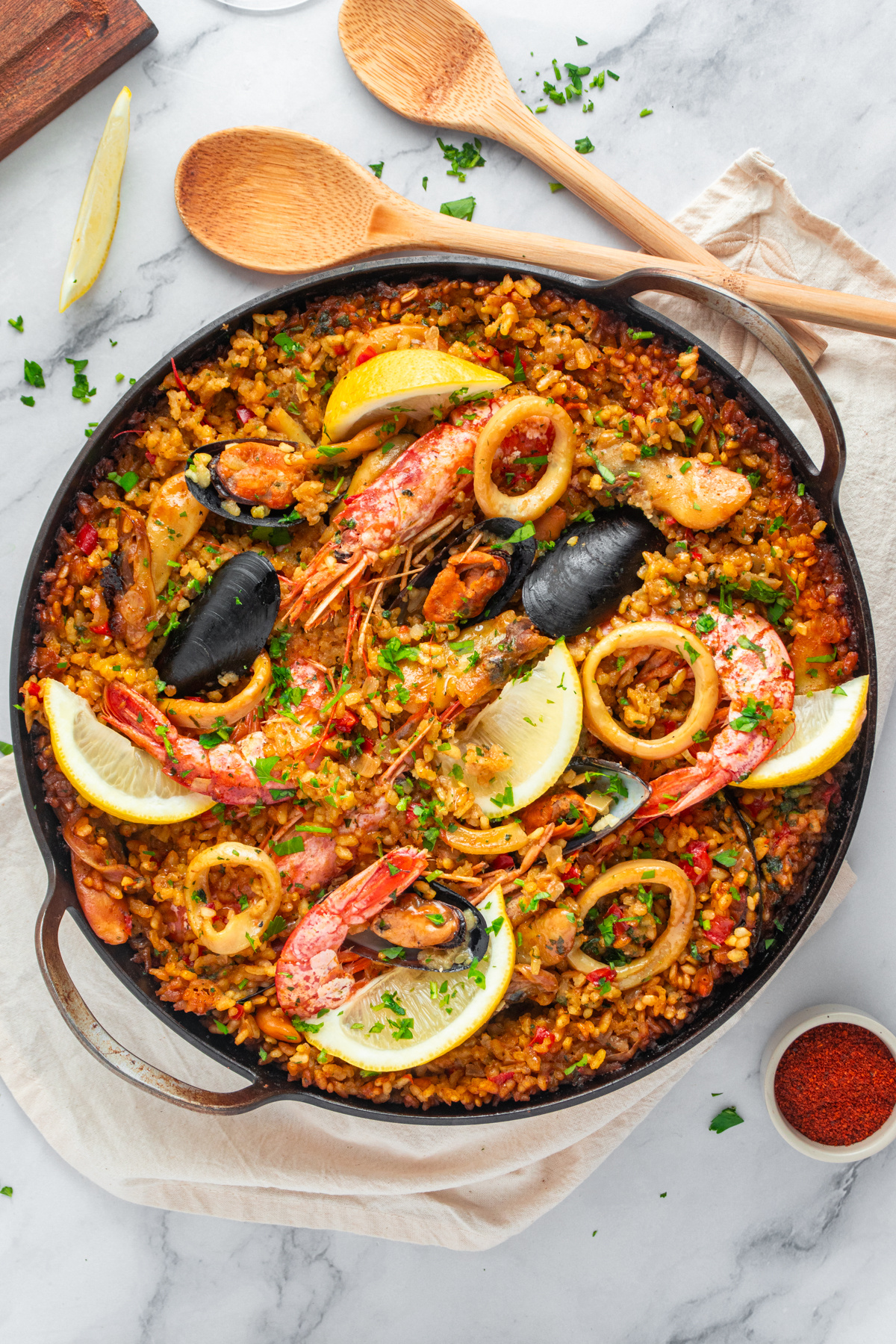 Seafood paella ready to serve. Garnish with chopped parsley and lemon wedges.