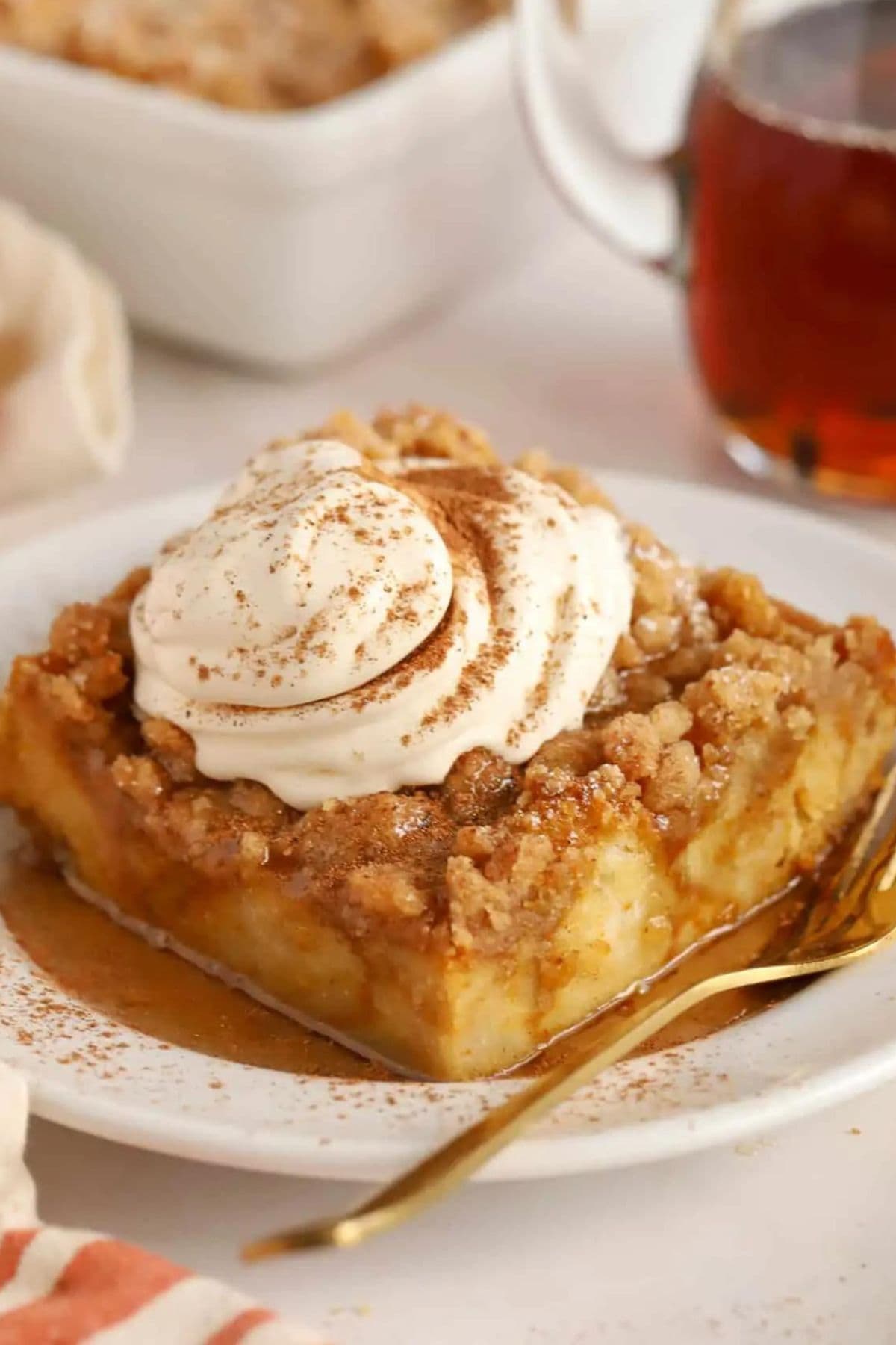 Slice of baked pumpkin french toast casserole on a small plate topped with whipped cream.