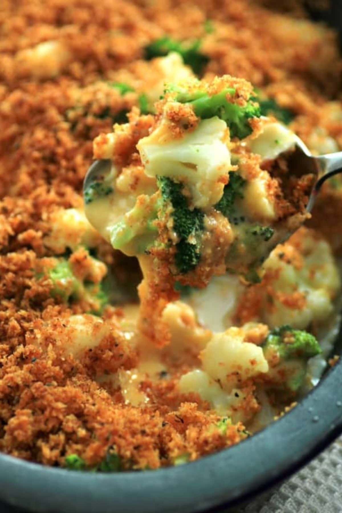 Spoonful of broccoli cauliflower cheese bake held above a casserole dish.