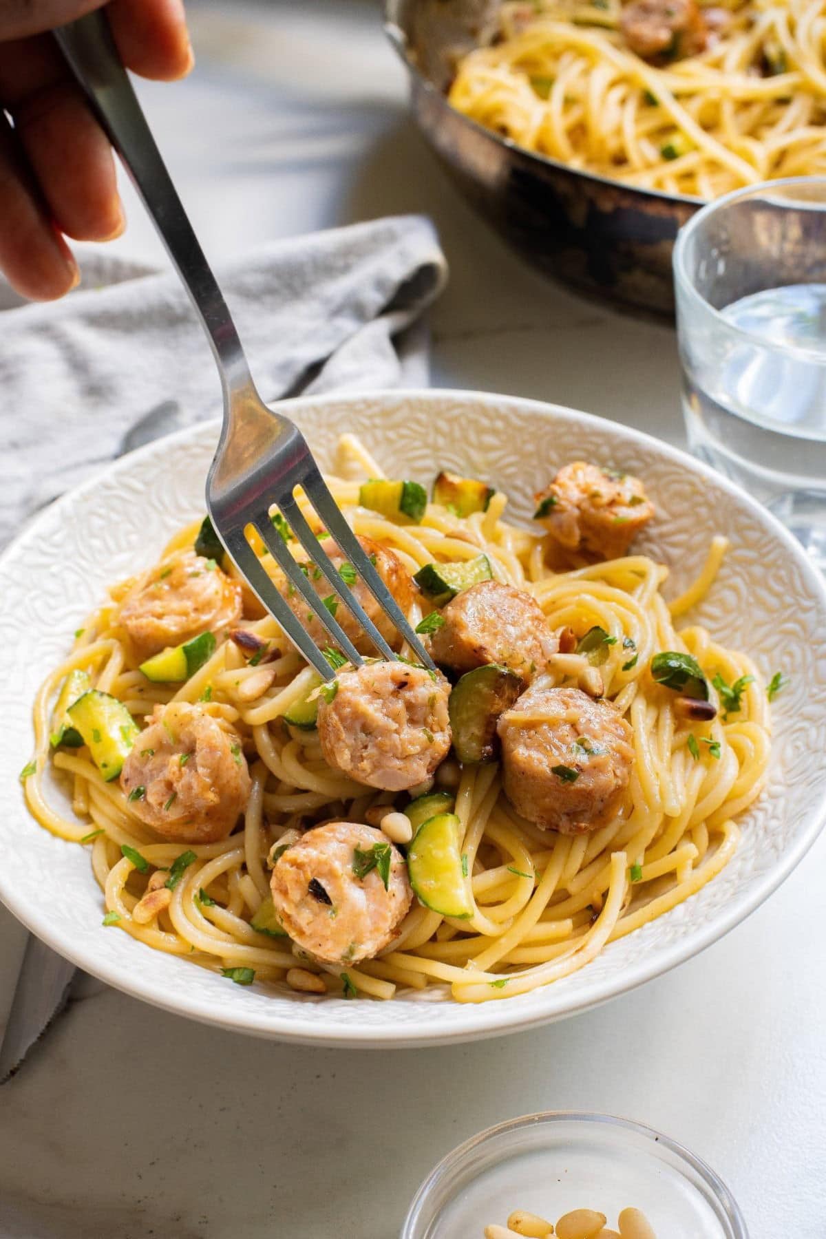 Bowl full of chicken sausage pasta, with a fork held in a woman's hand removing a bite.